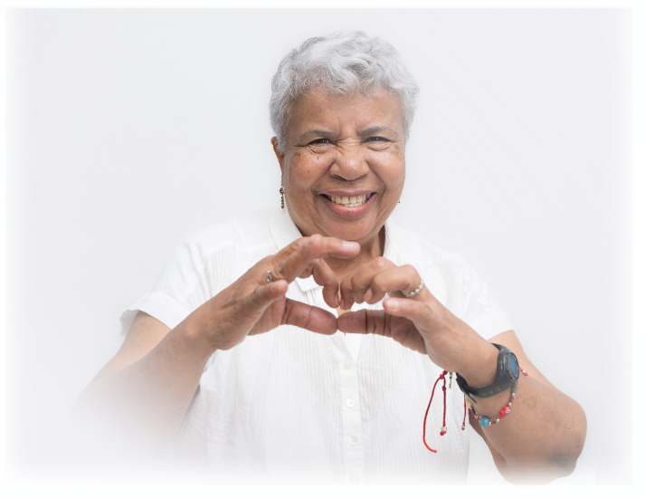 Envejeciente sonriendo y realizando un corazón con sus manos.